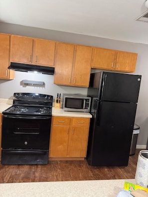 Una cocina con gabinetes de madera, una estufa negra, un microondas y un refrigerador.