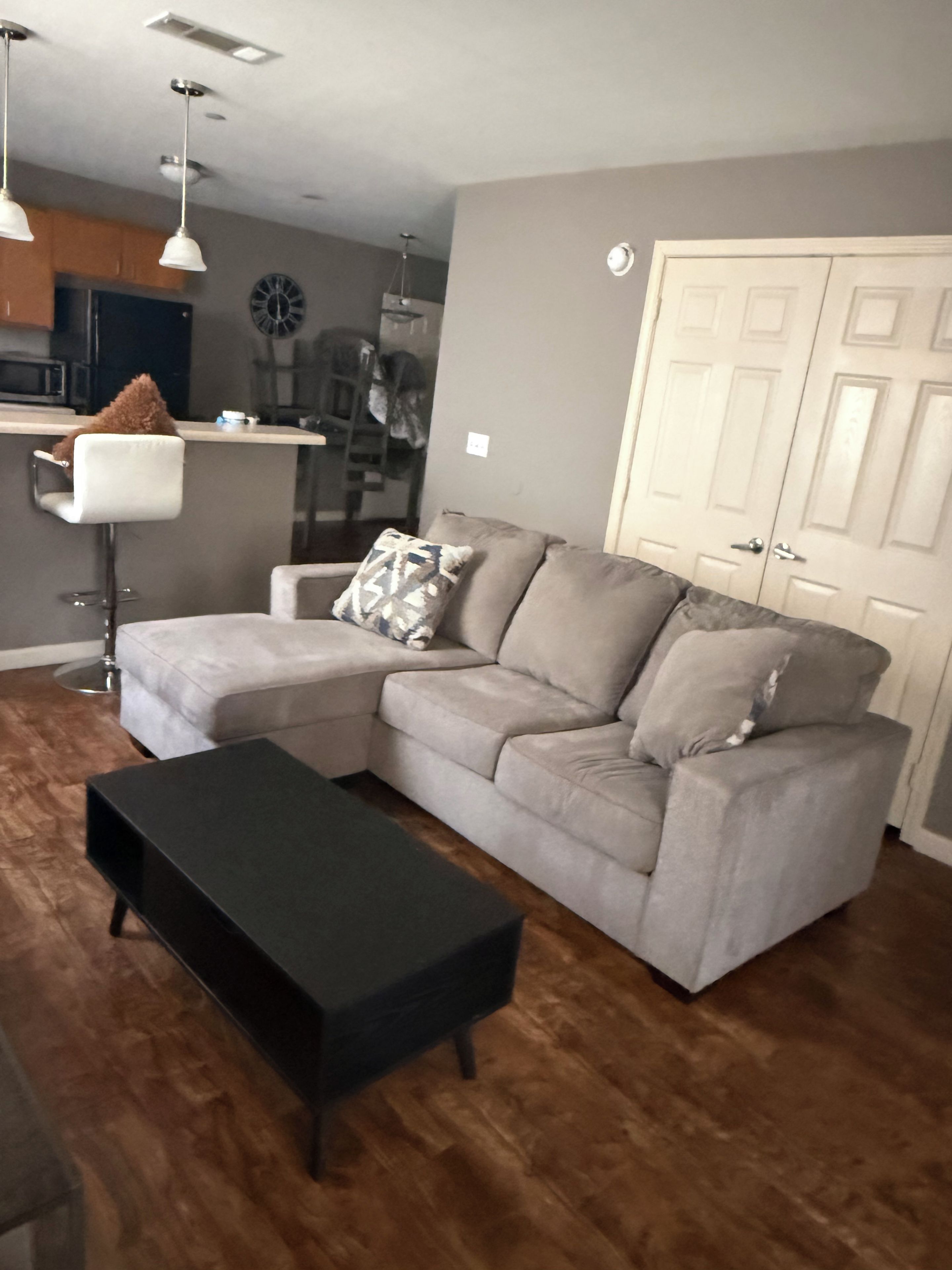 A living room with a sectional sofa, a black coffee table, and a kitchen area in the background.