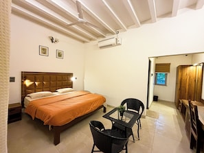 A hotel room with a bed, a table with chairs, a ceiling fan, and an air conditioning unit.