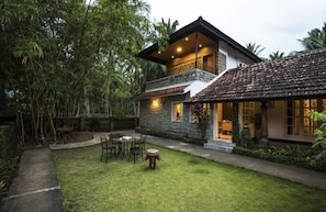 A two-story house with a stone facade, a balcony, and a well-maintained lawn. - Ibex Resorts Sethumadai -Banyan Tree (Sethumadai)