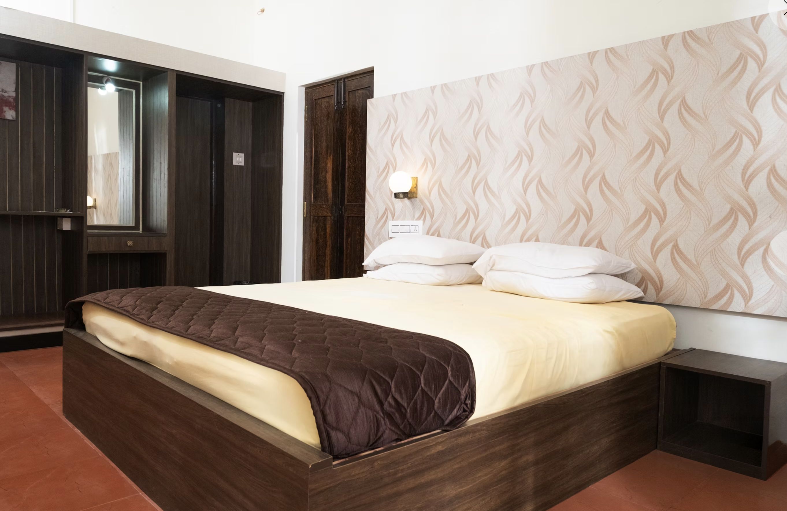Un dormitorio con cama, mesita de noche, armario y una lámpara de pared.