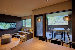 A modern interior with a wooden dining table, cushioned seating, and large windows offering a view of the outdoors. - Rakuten STAY VILLA Furano (Furanoshi)