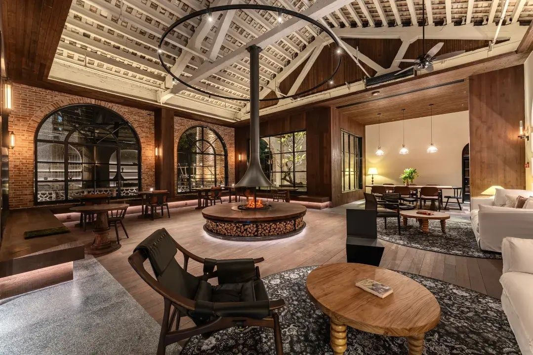 A spacious lobby with a central fire feature, seating areas, and large windows.