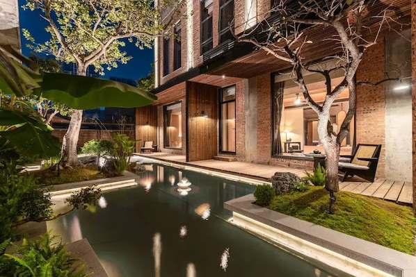 A modern building with a swimming pool, outdoor seating, and trees.