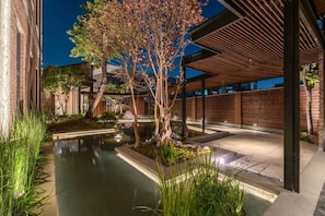 A modern outdoor area with a water feature, wooden pergola, and a brick building.