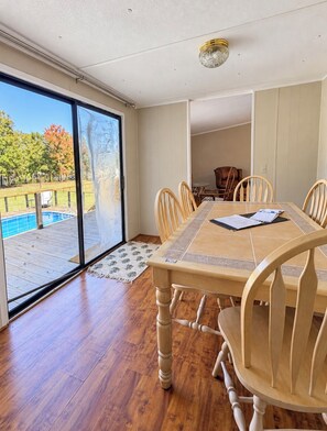 A dining area with a large table, wooden chairs, and a view of a swimming pool through a glass door.