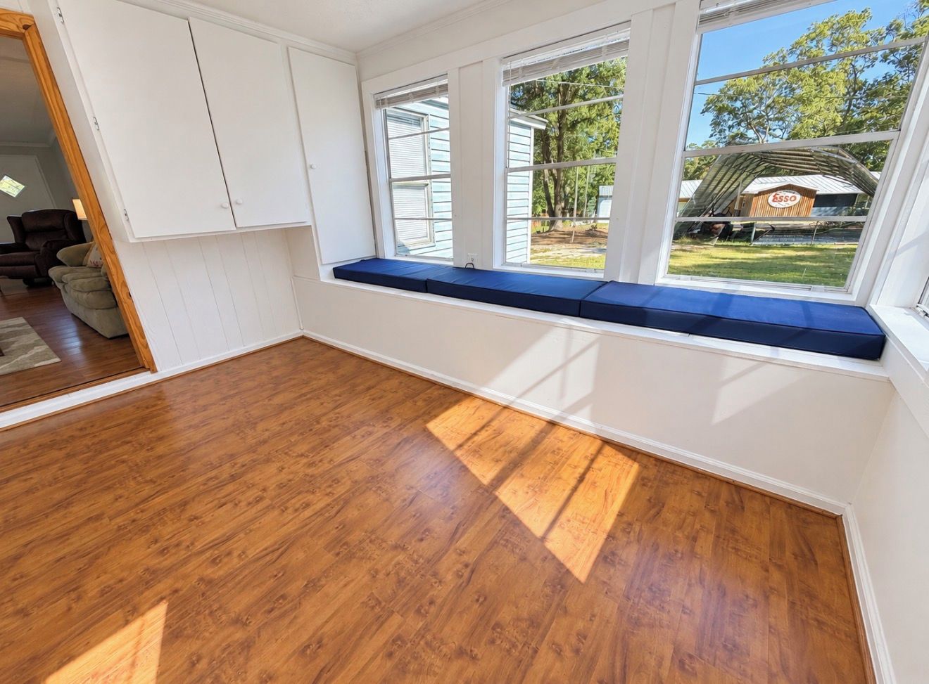 A room with a large window, wooden flooring, and a built-in bench.