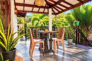 Eine Terrasse im Freien mit Tisch und Stühlen, umgeben von Blumentöpfen und Blick auf üppiges Grün.