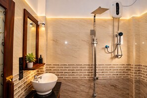 Un baño moderno con suelo de mármol, un lavabo blanco, una ducha con cabezal de ducha manual y un panel de control empotrado en la pared.
