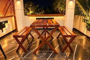 Un área de comedor al aire libre con una mesa y bancos de madera, rodeada por un muro blanco y plantas.