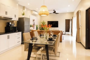 A modern kitchen with white cabinets, a black refrigerator, and a dining area with a glass table set for four. - Secluded 3BR Pool Villa near Nai Harn Rawai (Tambon Rawai)