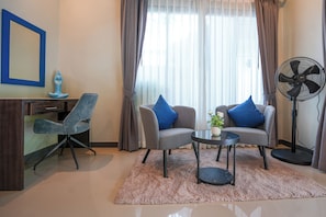 Een moderne woonkamer met een bank, fauteuil, salontafel en een staande ventilator.