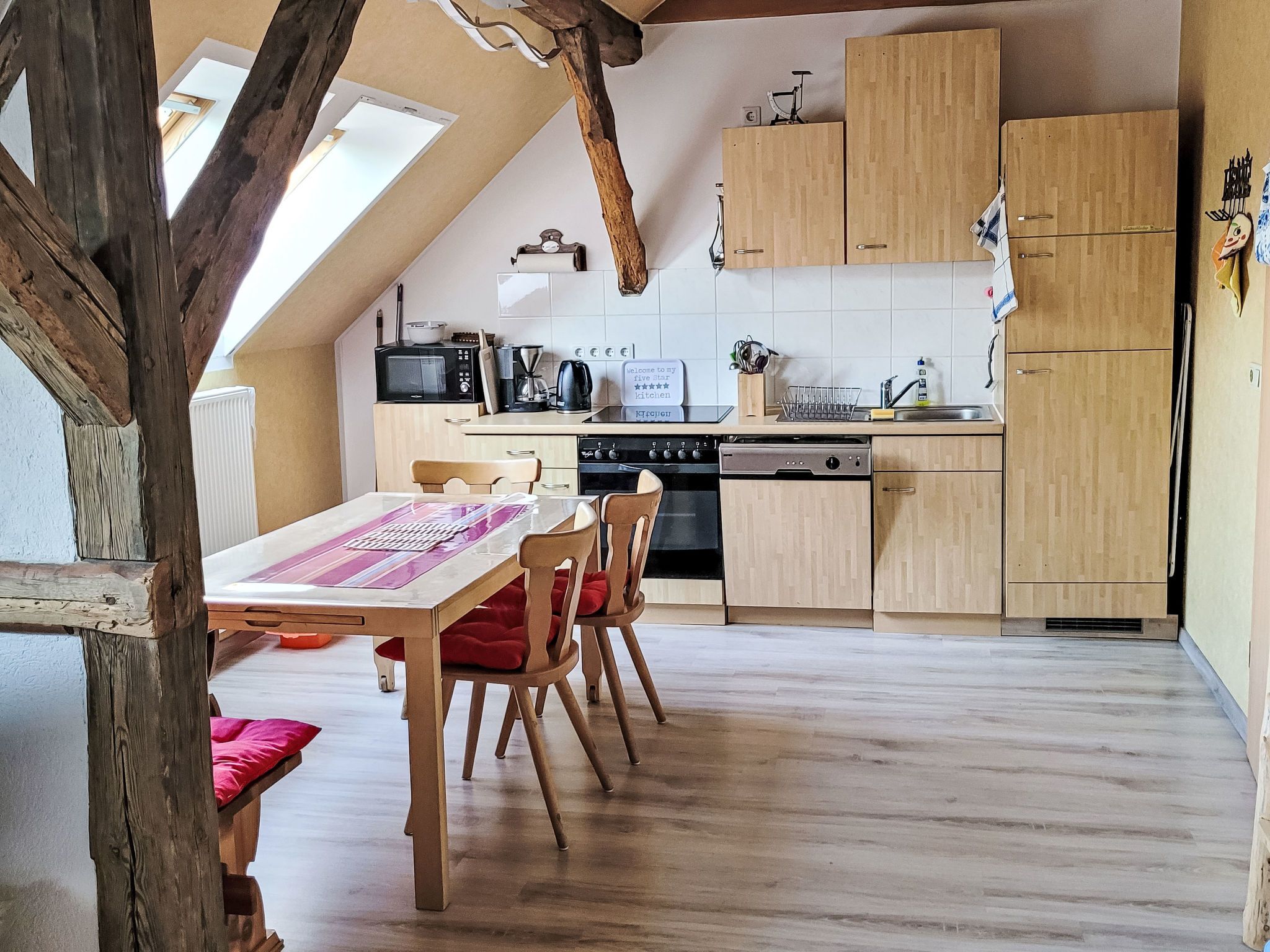 Une cuisine avec des meubles en bois, une table à manger avec des chaises et une vue sur l’extérieur.