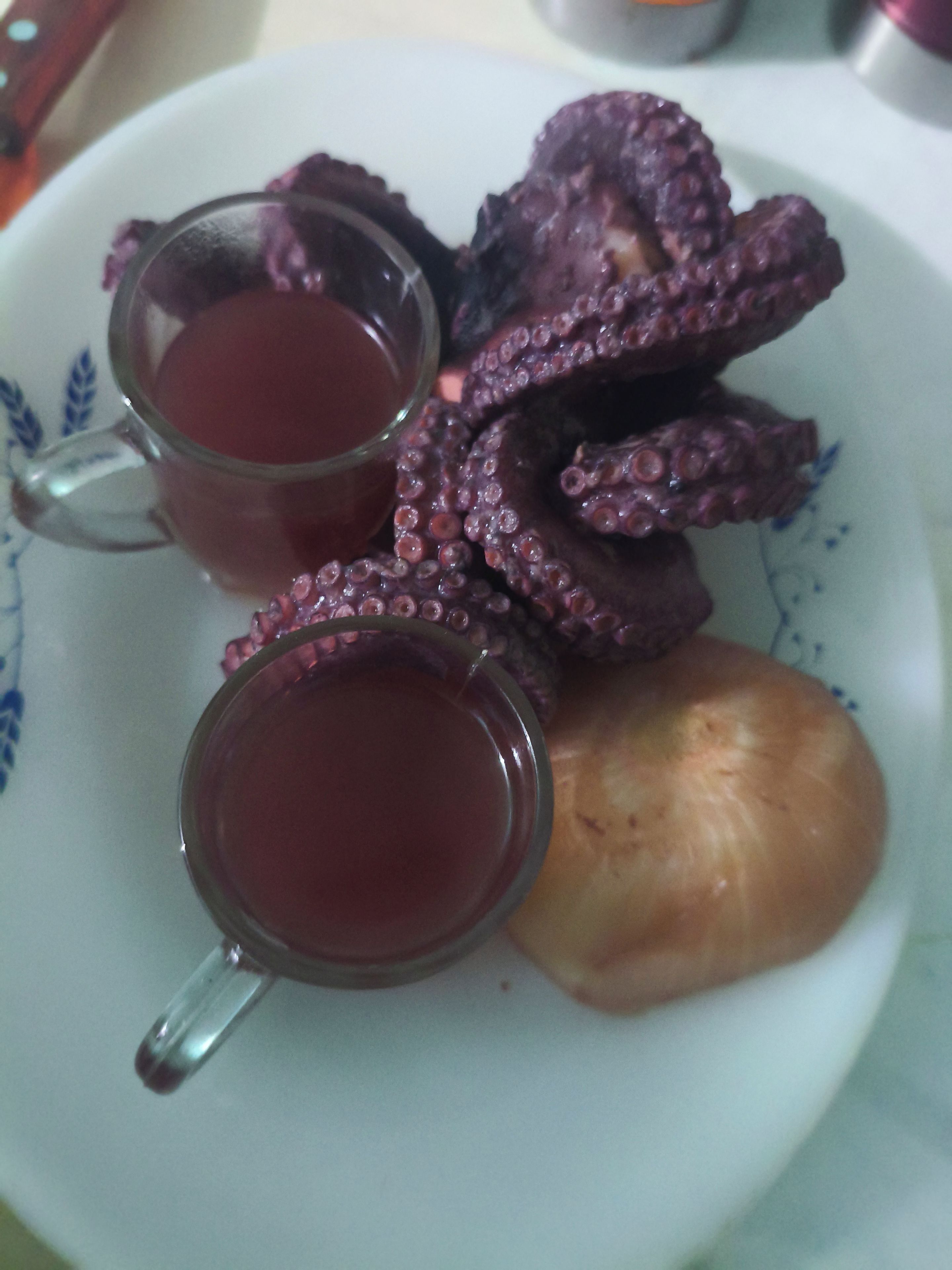 Une assiette avec des tentacules de poulpe et deux verres contenant un liquide rouge, probablement du thé.