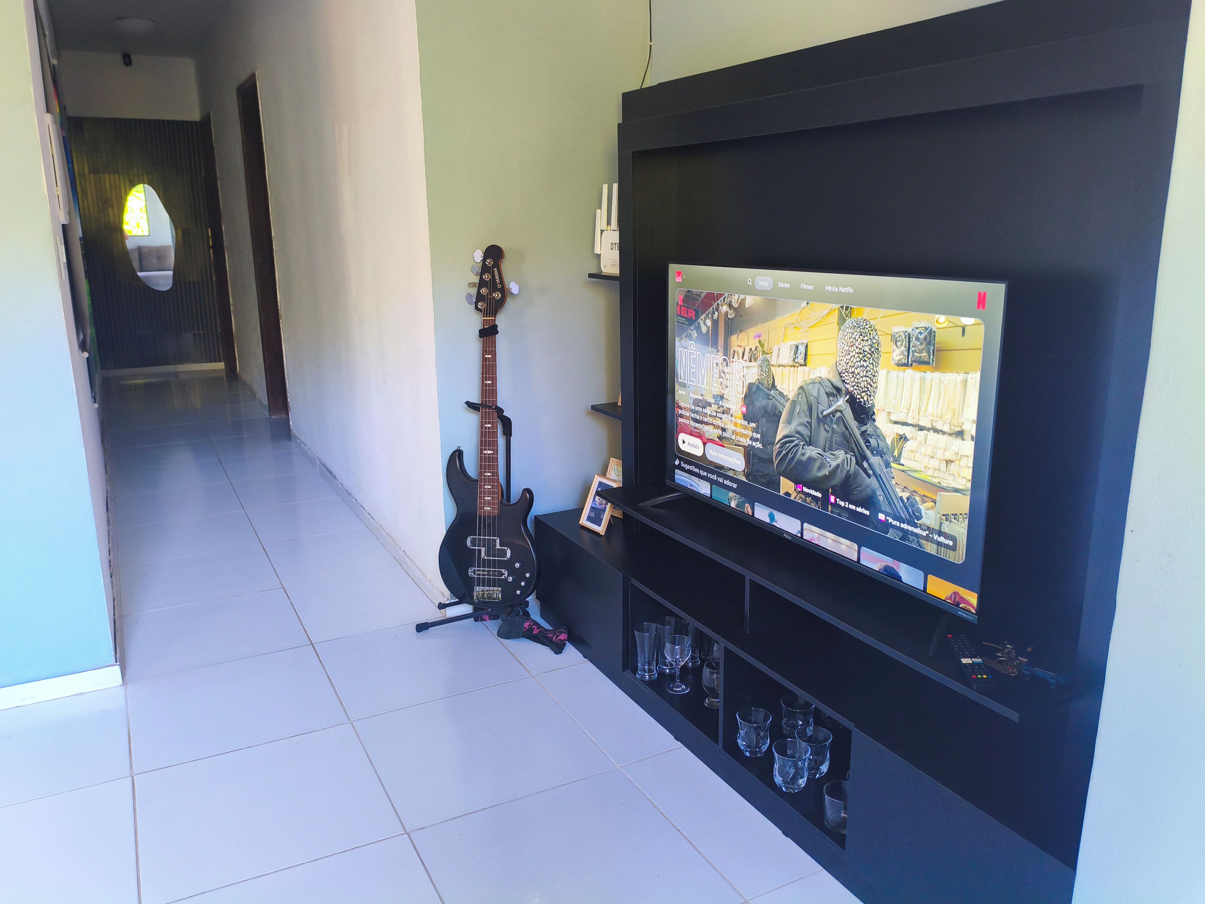 A living room with a television mounted on the wall, a guitar, and a shelf with glasses.