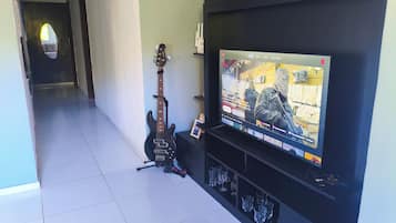 A living room with a television mounted on the wall, a guitar, and a shelf with glasses.
