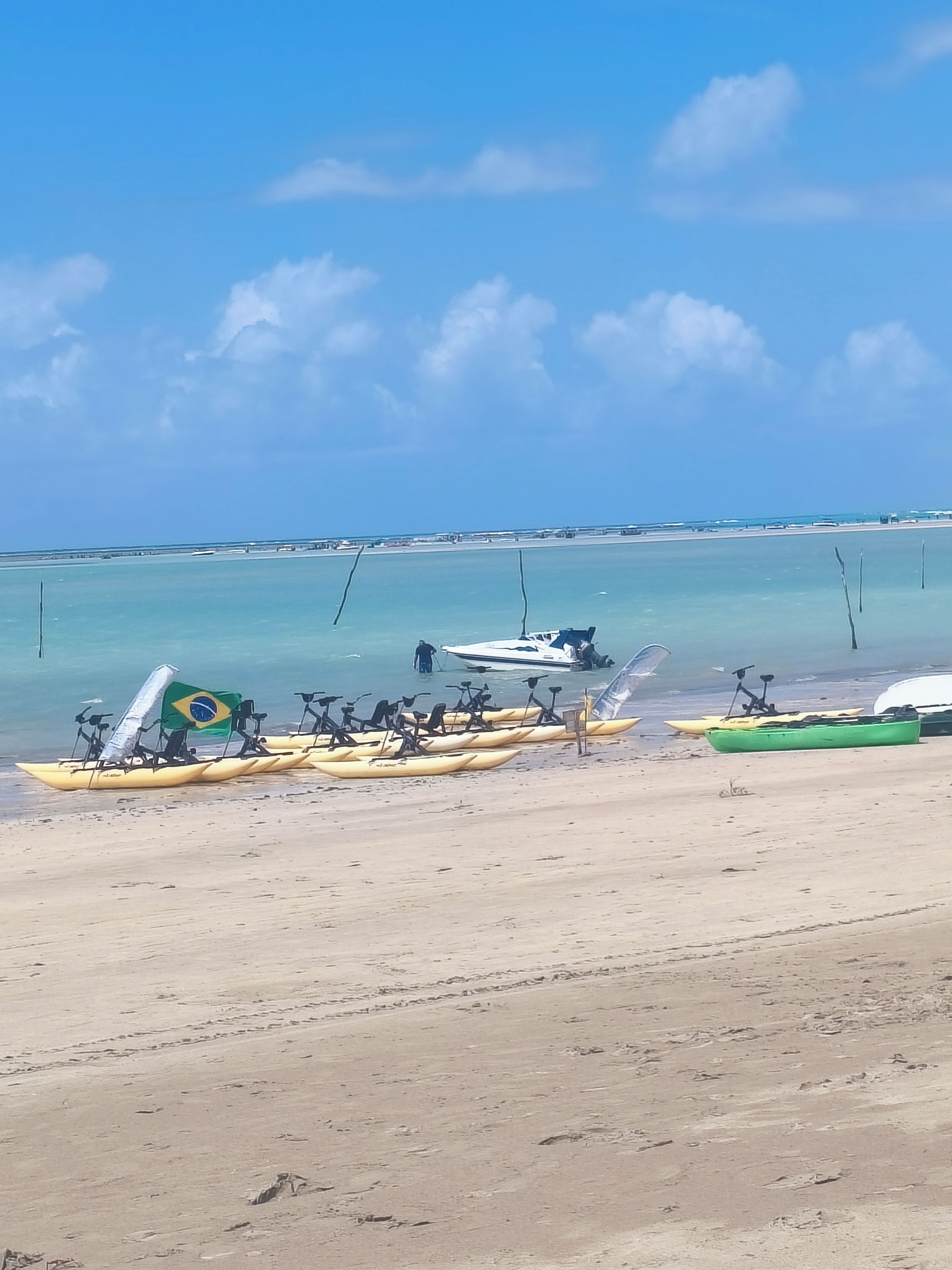 A beach with kayaks and a boat, clear skies, and calm water.