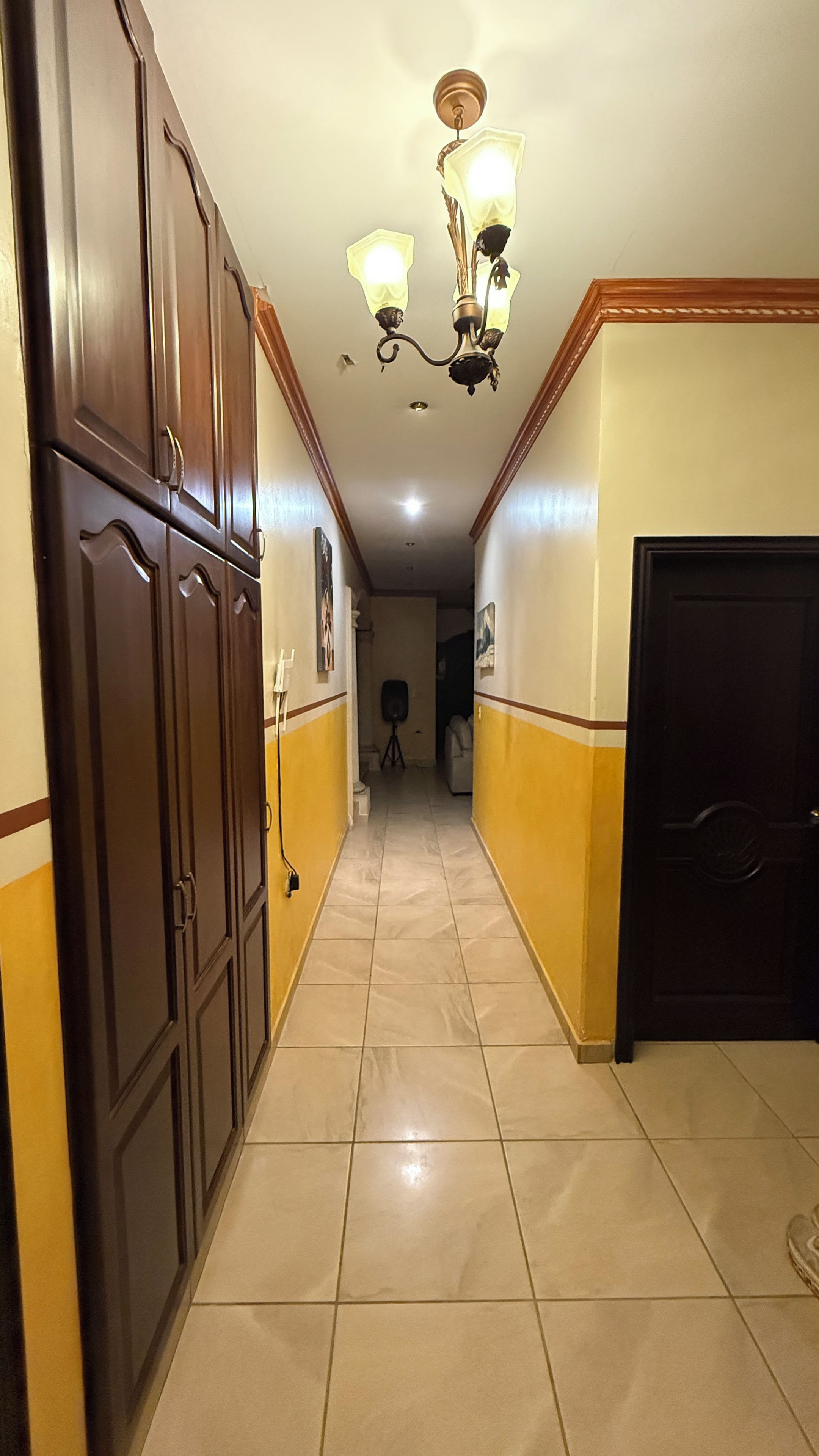 A hallway with a chandelier, wooden cabinets, and a door.