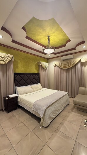 A spacious bedroom with a large bed, a nightstand, a chair, and a ceiling with a decorative design. - New Listing (Puerto Cortés)