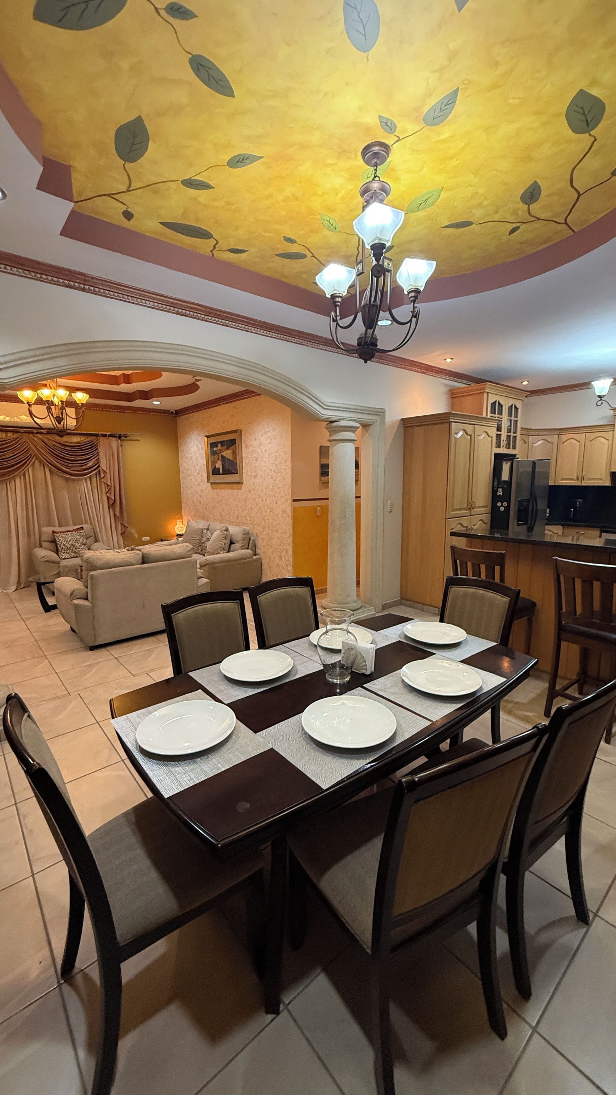 Un comedor con una mesa preparada para cuatro, una araña y una cocina al fondo.