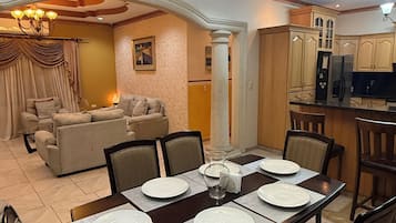 Un comedor con una mesa preparada para cuatro, una araña y una cocina al fondo.