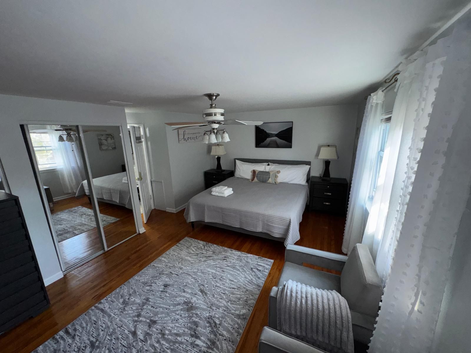 A bedroom with a bed, bedside tables, a mirror, a ceiling fan, and a window with curtains.