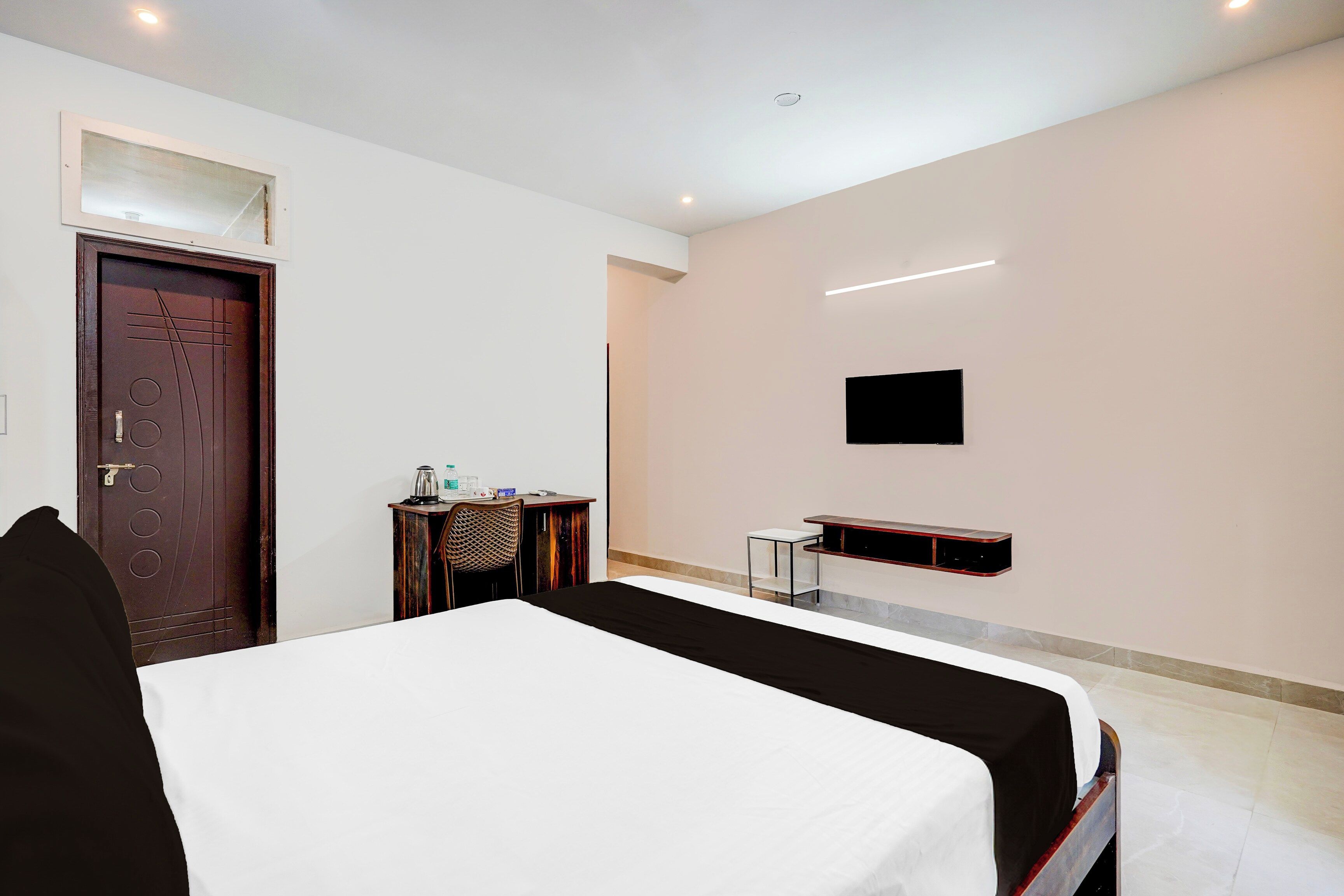 A hotel room with a bed, a desk, a chair, a television mounted on the wall, and a door.
