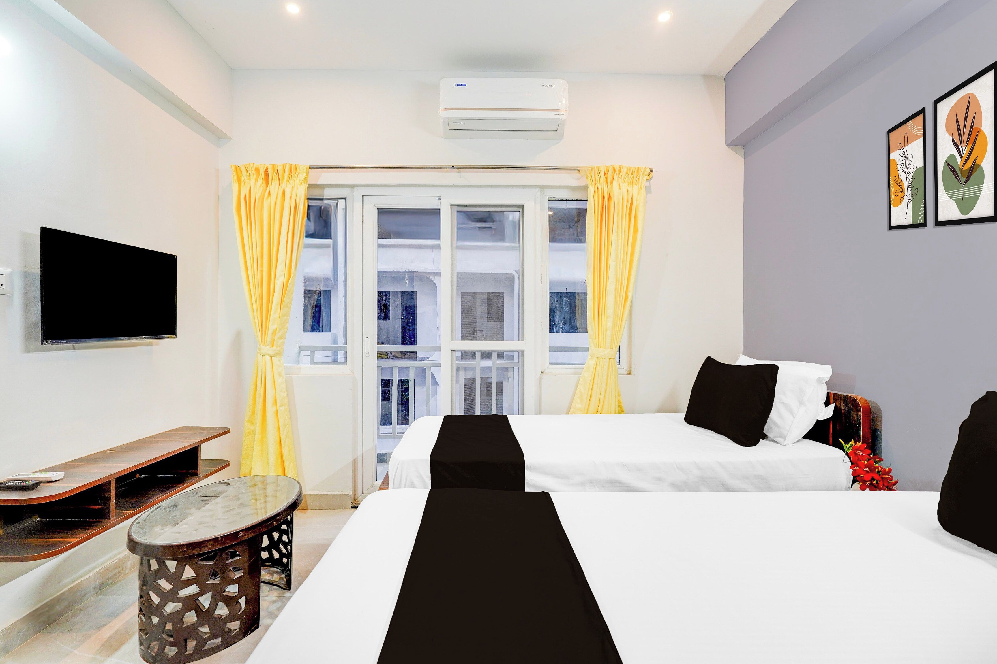 A hotel room with two beds, a flat-screen TV, a small table, and a window with curtains.