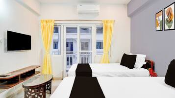 Quarto de hotel com duas camas, uma TV de tela plana, uma mesinha e uma janela com cortinas.