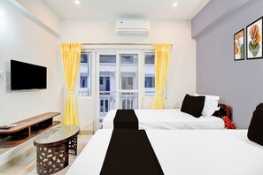 A hotel room with two beds, a flat-screen TV, a small table, and a window with curtains. - Townhouse Jeevith Gardens Residency (Bangalore)