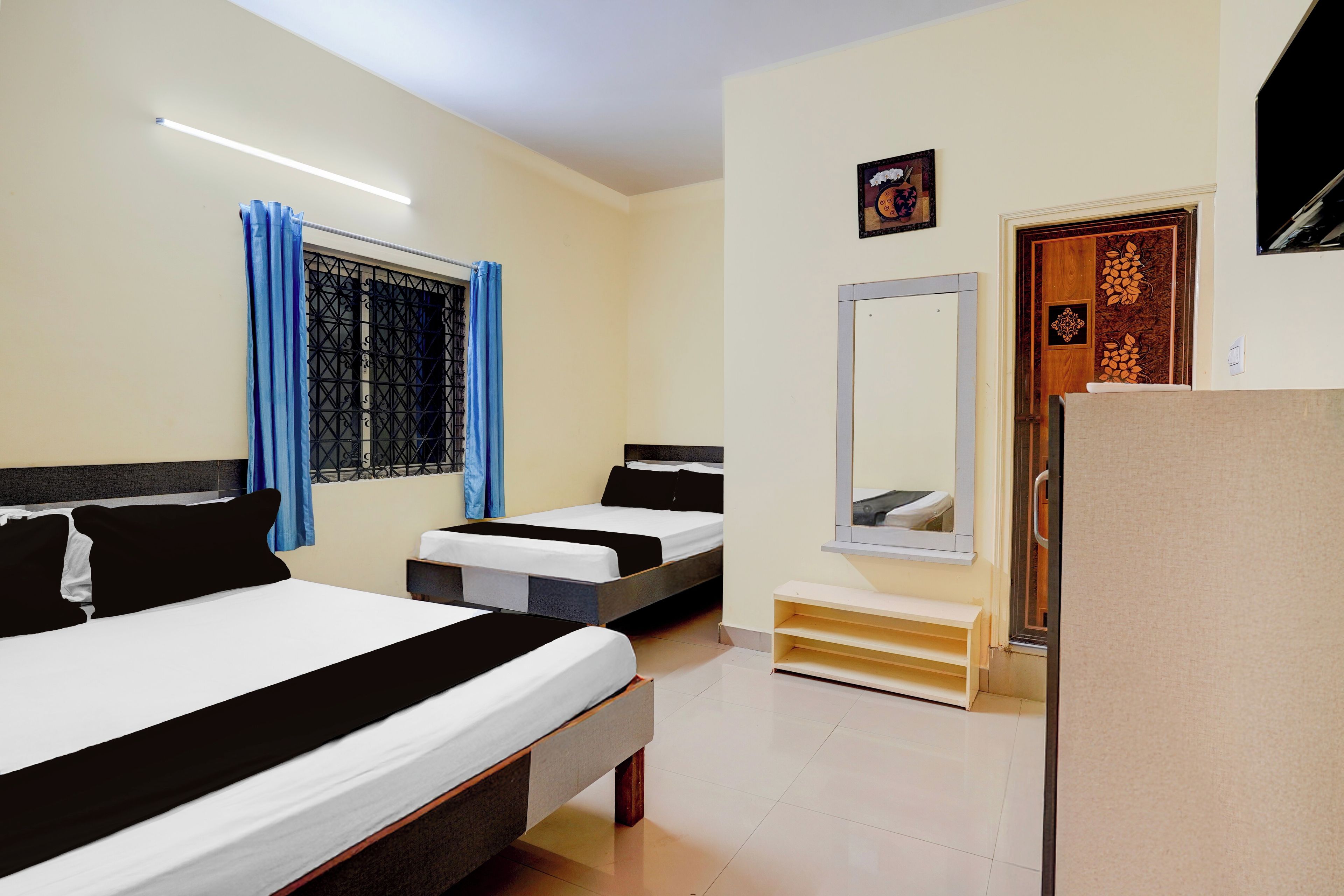 Habitación de hotel con dos camas, un pequeño banco, un espejo y una puerta con paneles decorativos.
