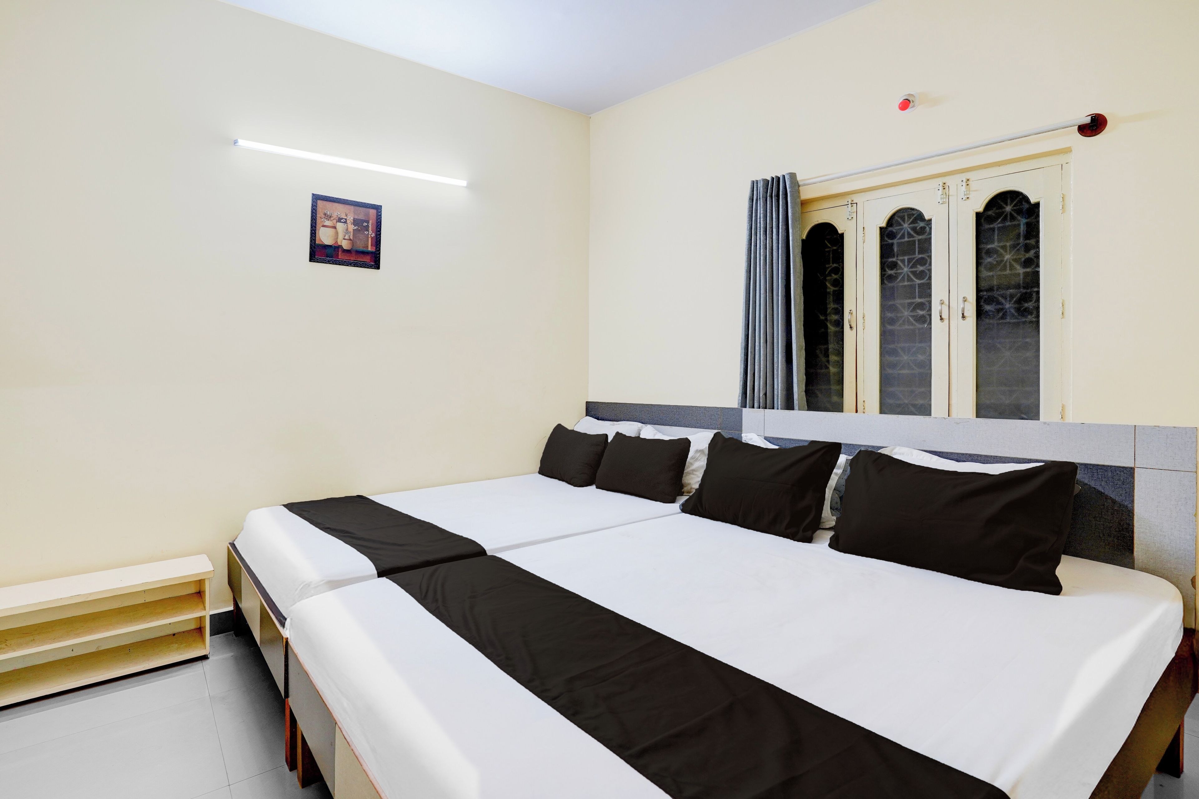 Una cama doble con ropa de cama blanco y negro, una mesita de noche pequeña y una ventana con cortinas.