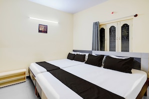 A double bed with black and white bedding, a small bedside table, and a window with curtains. - Hotel O Bluestar (Bangalore)
