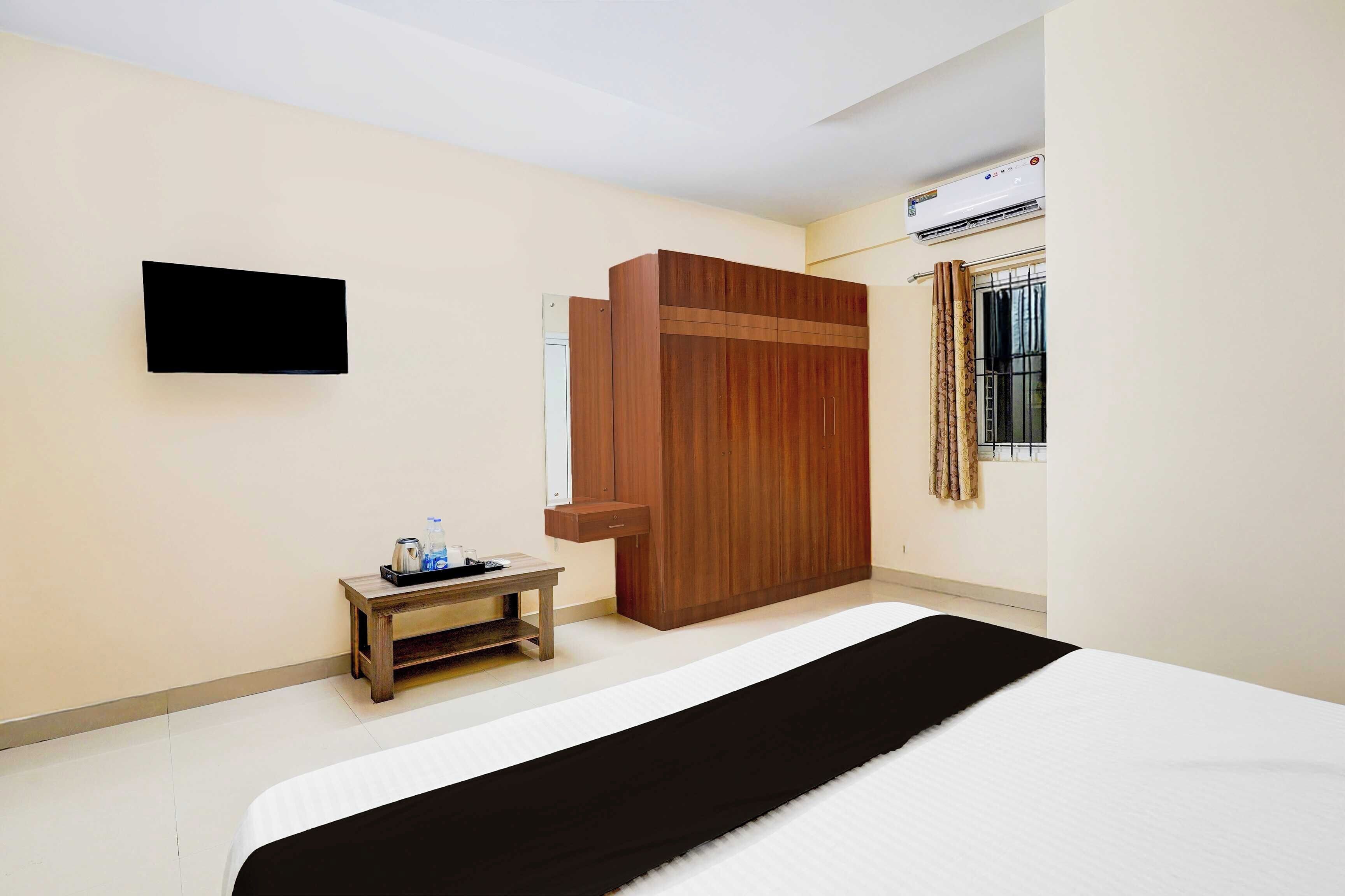 A hotel room with a bed, a small table with a tray, a wardrobe, a flat-screen TV, and an air conditioning unit.