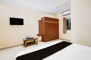 Een hotelkamer met een bed, een klein tafeltje met dienblad, een kledingkast, een flatscreen televisie en een airconditioner.