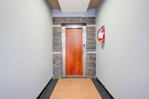 A hallway with a wooden door, a fire extinguisher on the wall, and a textured floor. - Hotel O Blueberry Hotels & Restaurant (Bangalore)