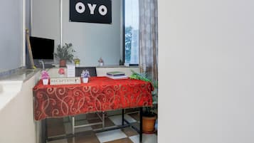 Uma área de recepção com uma mesa estampada em vermelho, um aviso indicando que garrafas de água e creme dental estão disponíveis, e um letreiro com 'OYO' na parede.