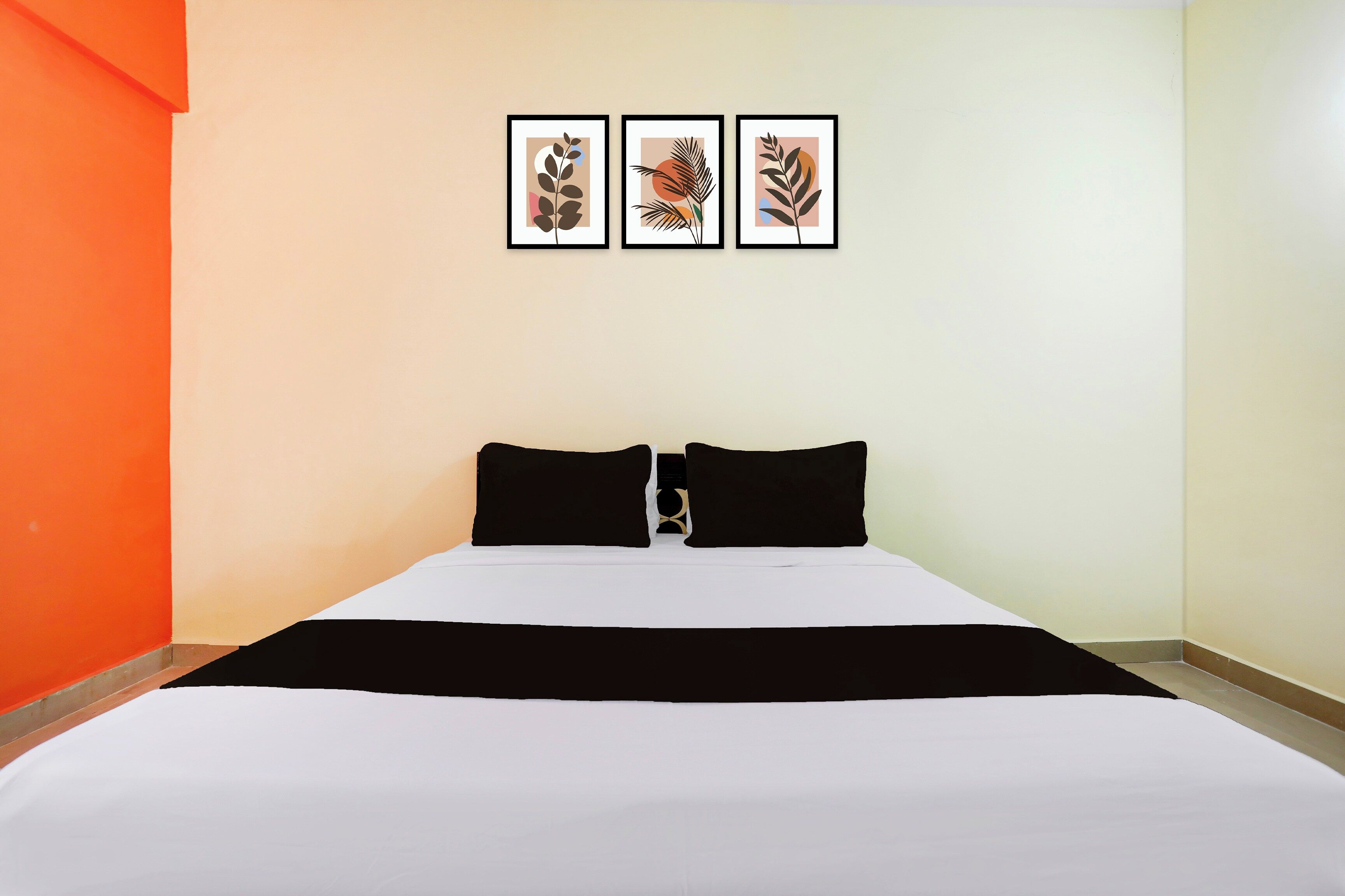 A hotel room with a bed, two black pillows, and three framed artworks on the wall.
