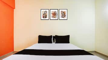 A hotel room with a bed, two black pillows, and three framed artworks on the wall.