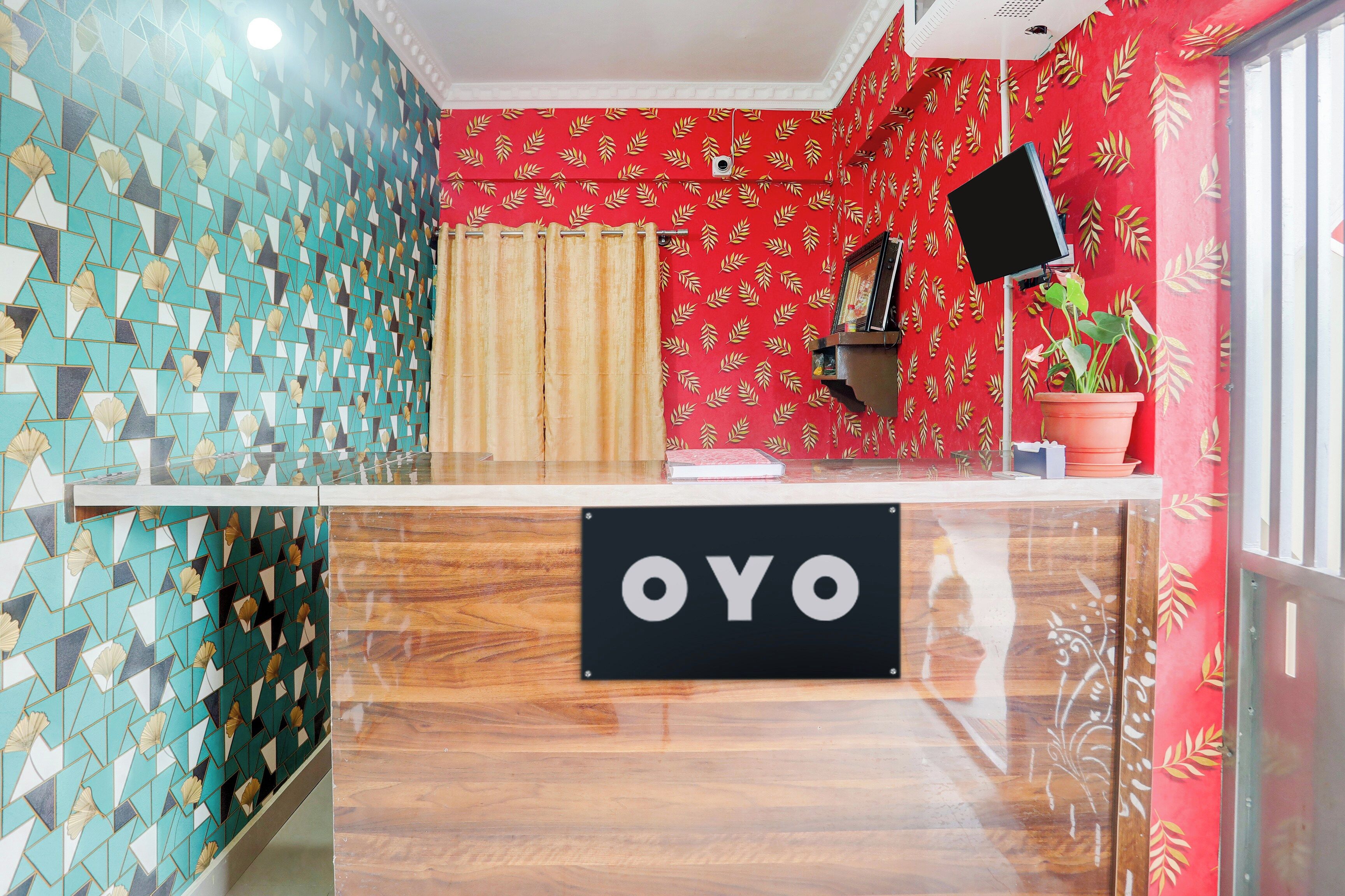 Un área de recepción con mostrador de registro, una pared con diseño rojo y una planta en maceta.