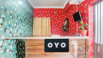 Un área de recepción con mostrador de registro, una pared con diseño rojo y una planta en maceta.