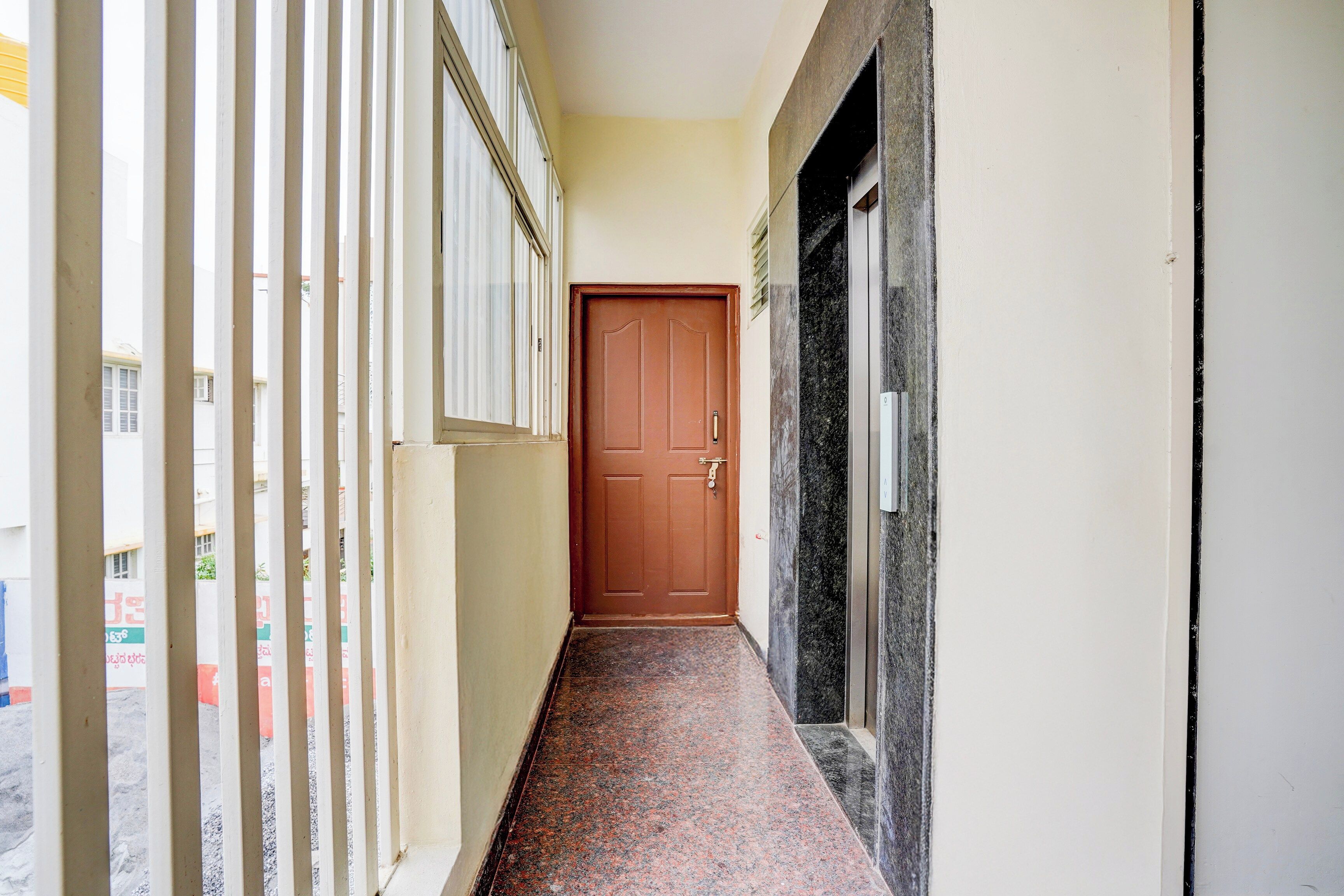Un couloir se terminant par une porte en bois, un sol carrelé et un mur blanc bordé de noir.