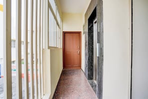 A corridor with a wooden door at the end, a tiled floor, and a white wall with a black border. - Hotel O SRL Comforts (Bangalore)