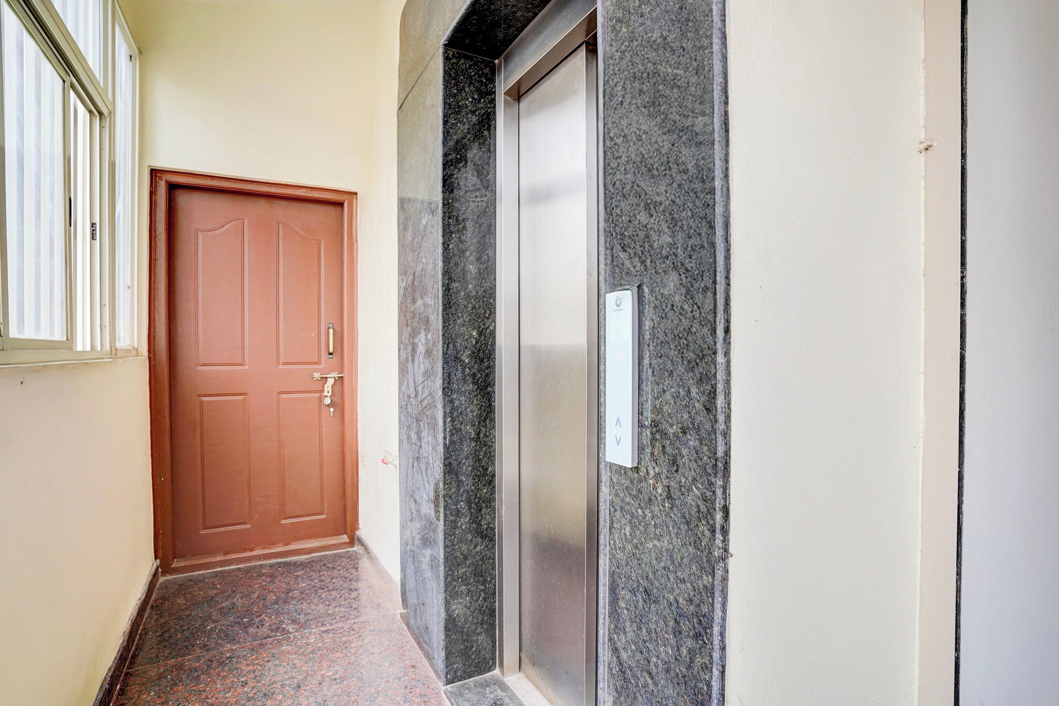 Un couloir avec une porte en bois, un mur en marbre et un carillon.