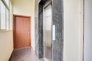 A hallway with a wooden door, a marble wall, and a doorbell. - Hotel O SRL Comforts (Bangalore)