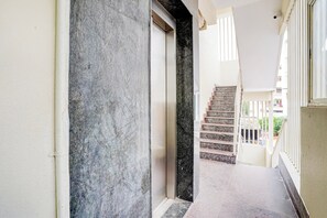 Un estrecho pasillo con una pared de mármol, una escalera de granito y una barandilla blanca.