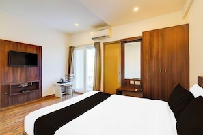 A hotel room with a bed, a TV, a desk, and a wardrobe. - Power Break Townhouse Whitefield (Bangalore)