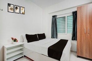 A bedroom with a bed, a wardrobe, a bedside table with a vase of flowers, and a window with curtains. - Hotel O by OYO Arrow Inn (Bangalore)