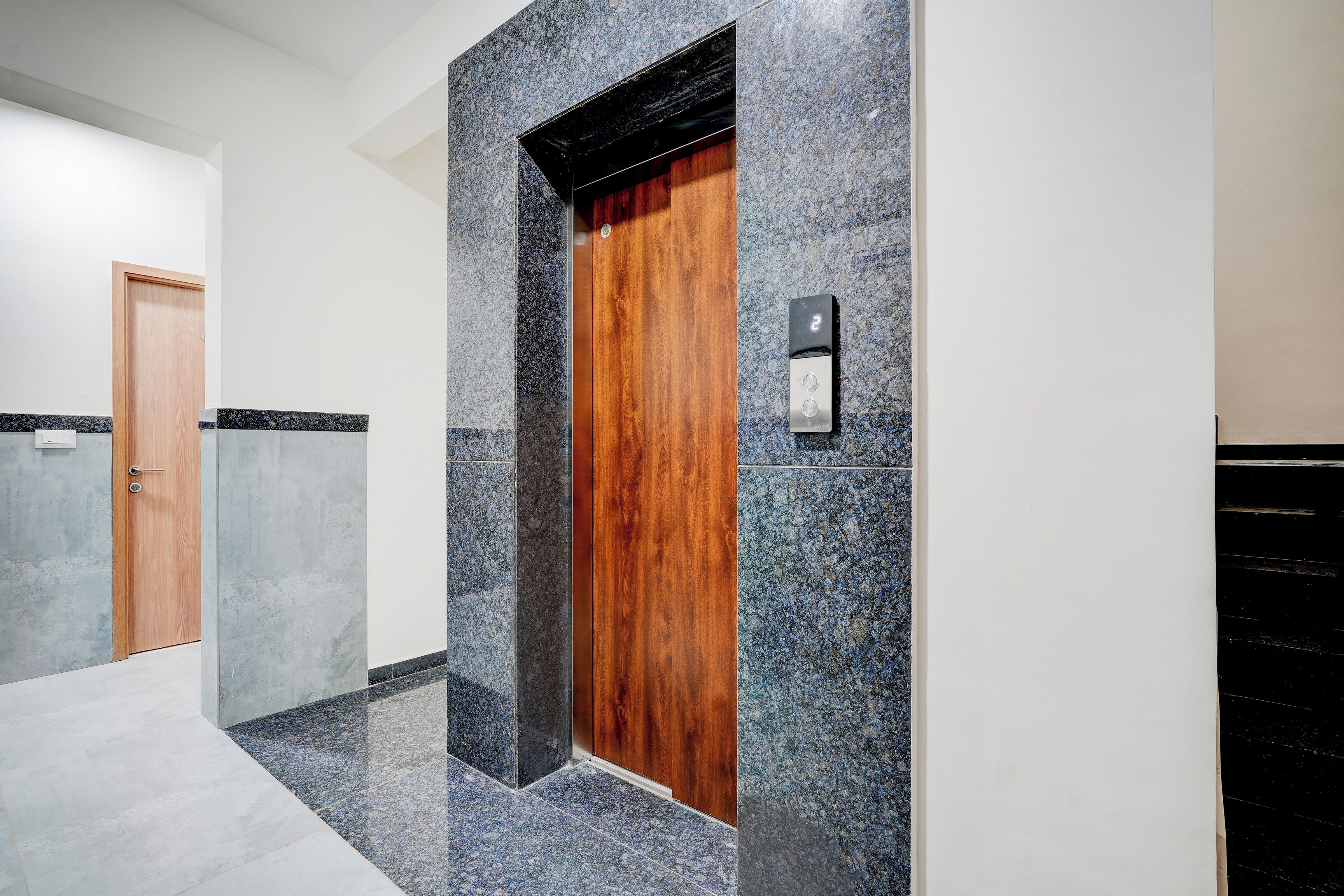 A hallway with a wooden door and a digital elevator control panel.