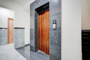 A hallway with a wooden door and a digital elevator control panel. - Hotel O by OYO Arrow Inn (Bangalore)